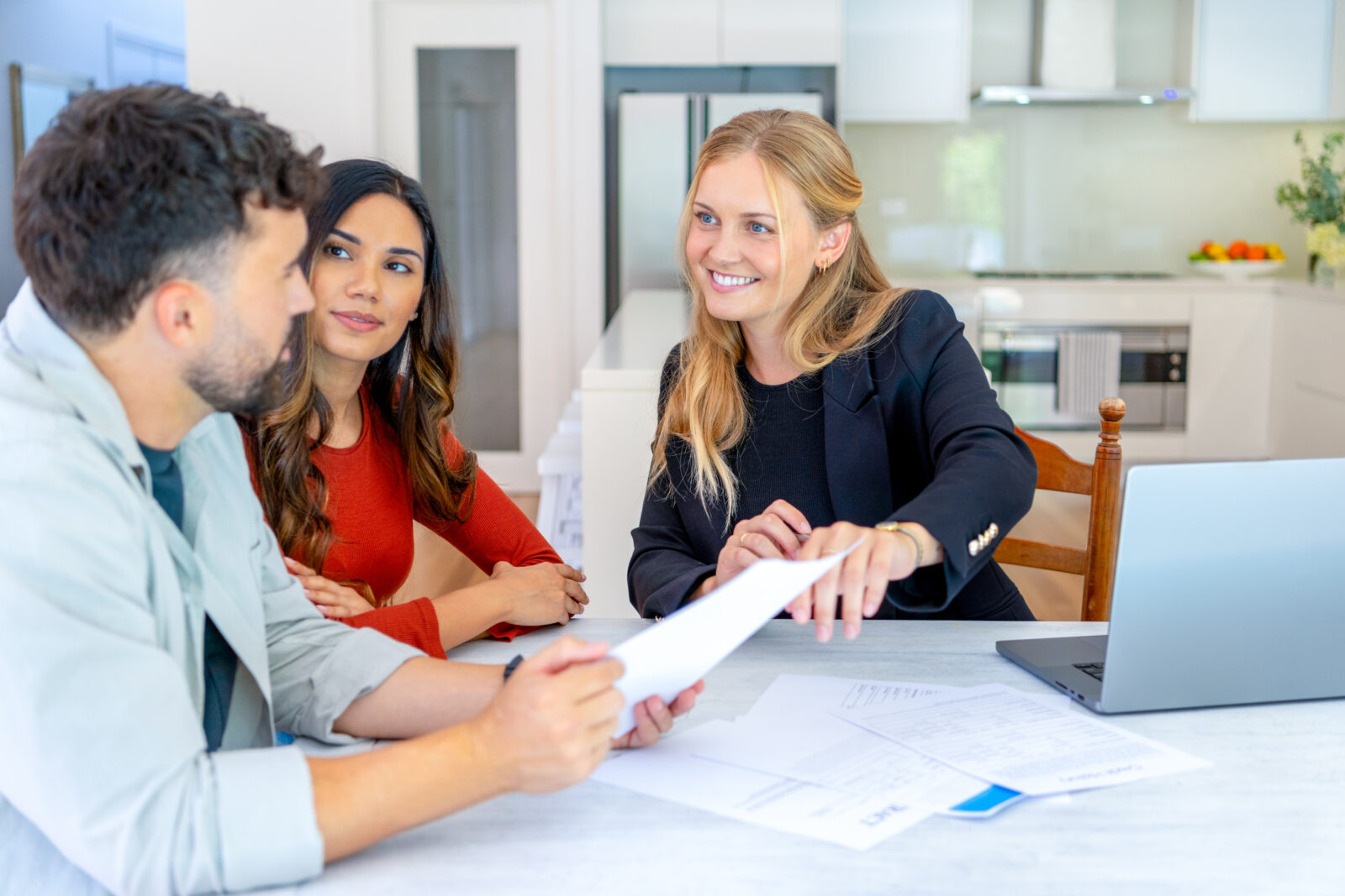 Makelaar bespreekt woningwaarde en vraagprijs met stel aan keukentafel