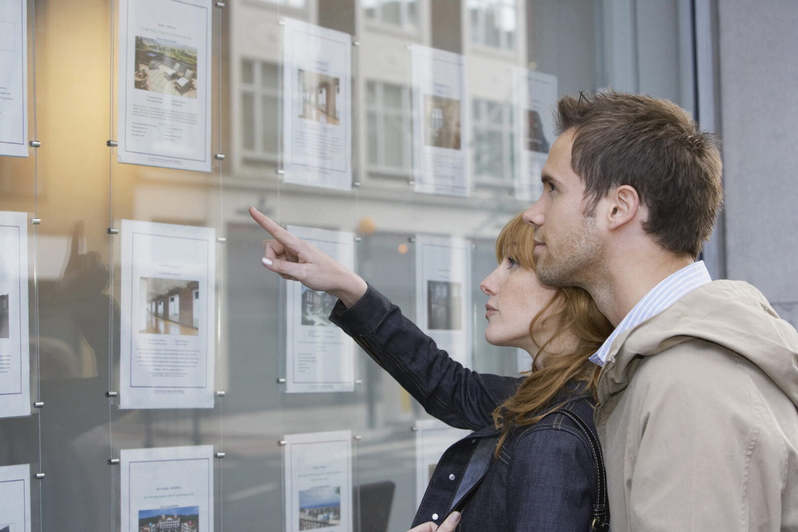 Stel bekijkt woningaanbod in de etalage van een makelaar