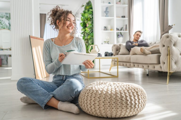 Vrouw maakt een planning in een stijlvol, licht interieur terwijl haar partner ontspannen op de bank zit