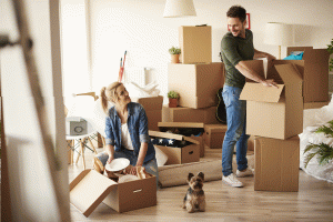 Een man en vrouw staan tussen verhuisdozen met hun hondje, klaar om te verhuizen