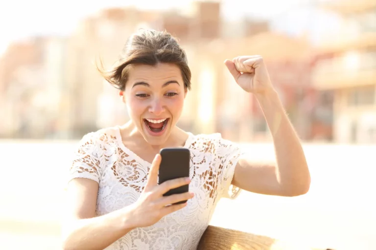 Vrouw reageert enthousiast op woningnieuws op haar telefoon na aankoop van een huis