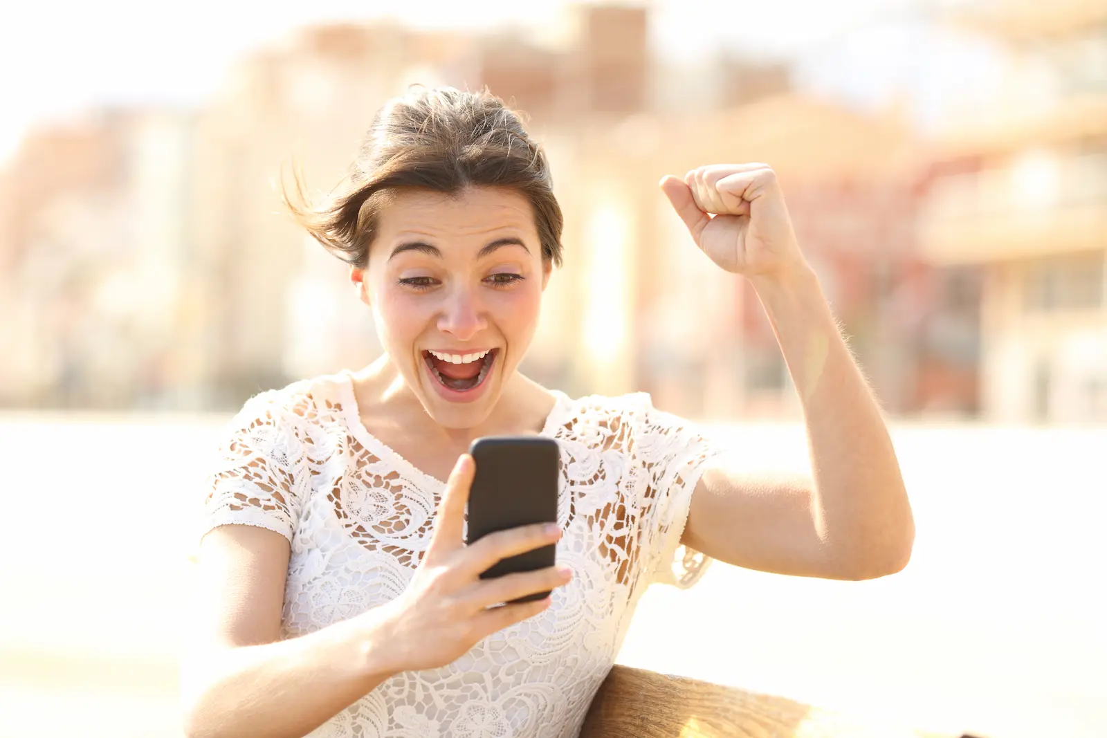 Vrouw reageert enthousiast op woningnieuws op haar telefoon na aankoop van een huis