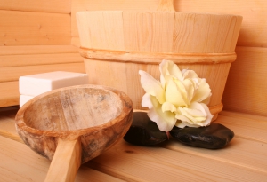 Sauna-accessoires met houten emmer, lepel, bloemen en zeep, rustend op een houten bank in een sauna.