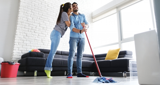 Een lachend stel dat samen de vloer schoonmaakt, waarbij de plinten en vloer netjes en schoon worden gehouden.