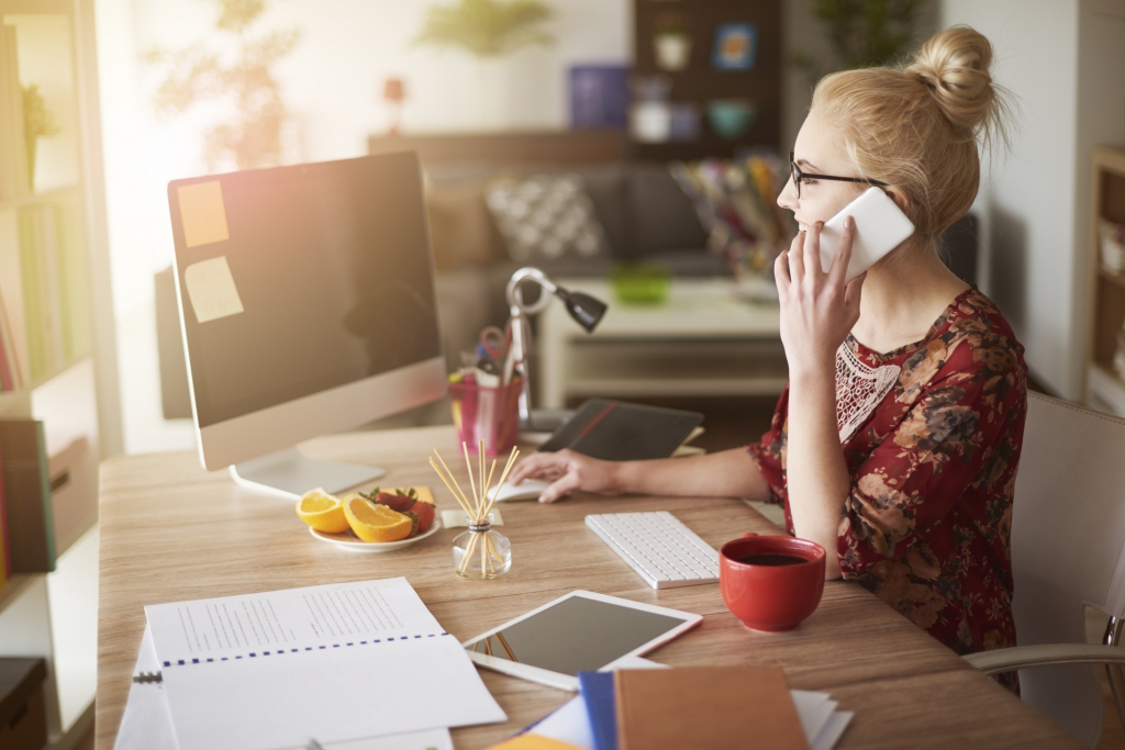 Vrouw personaliseert haar thuiskantoor met een houten bureau, kleurrijke decoratie, en een inspirerende werkplek terwijl ze aan het bellen is.g