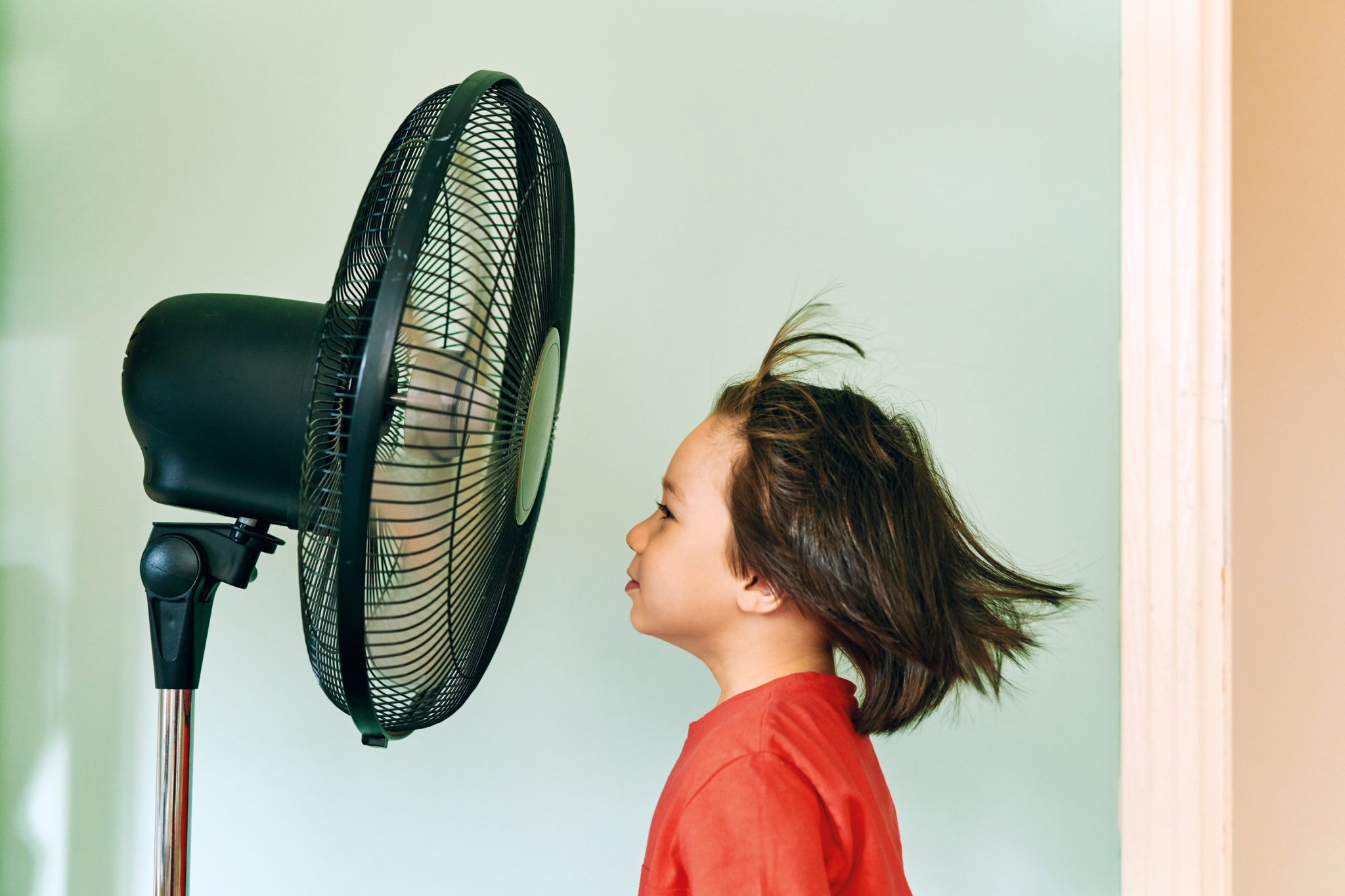 Een kind geniet van een perfecte bries terwijl het voor de ventilator staat – een ventilatiesysteem dat zijn werk goed doet!