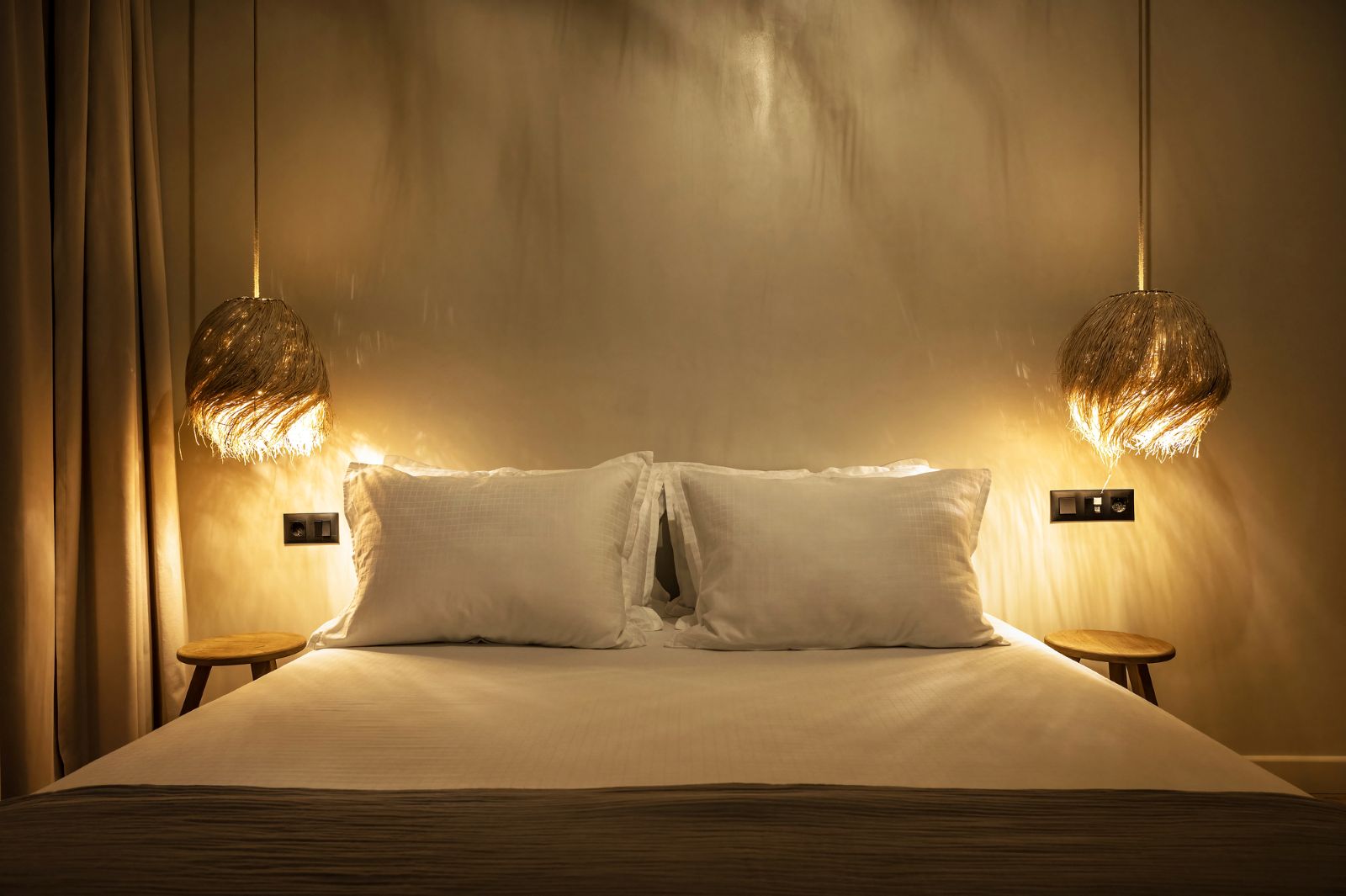 Twee hanglampen verspreiden warm licht aan weerszijden van een bed in een sfeervolle slaapkamer.