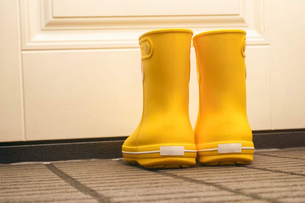 Gele regenlaarzen op een droogloopmat bij de voordeur