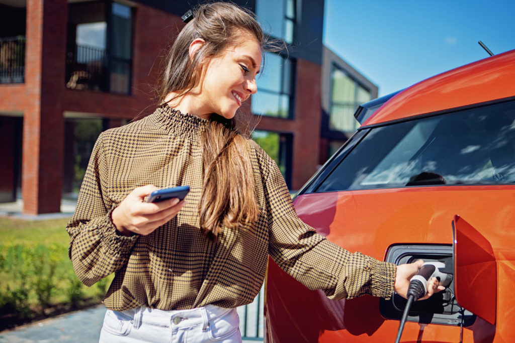 Vrouw laadt een elektrische auto op bij moderne woningen, een voorbeeld van de toenemende elektriciteitsvraag in huishoudens.