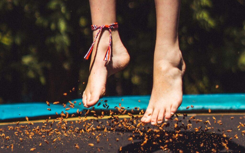 kind springt op trampoline met blote voeten in de tuin
