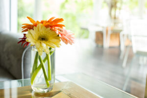 Close-up van een kleurrijke verzameling bloemen in een glazen vaas, met een mix van gele, oranje en rode Gerbera's. De achtergrond is zachtjes vervaagd, waardoor de heldere en vrolijke kleuren van de bloemen opvallen.