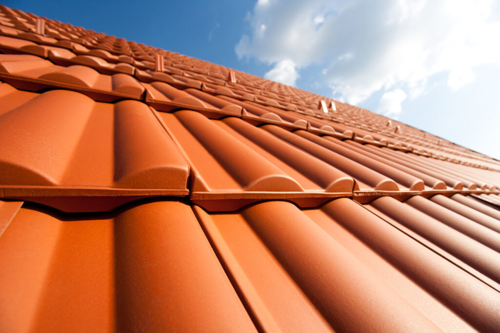 Nieuwe, oranje dakpannen onder een blauwe hemel, symbool voor een opgewaardeerd en duurzaam dak dat de waarde van een woning verhoogt.