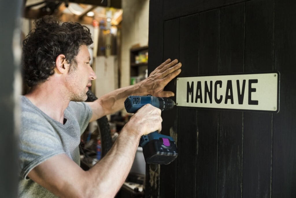 Man hangt mancave bord op in tuinhuis dat wordt ingericht als persoonlijke hobbyruimte