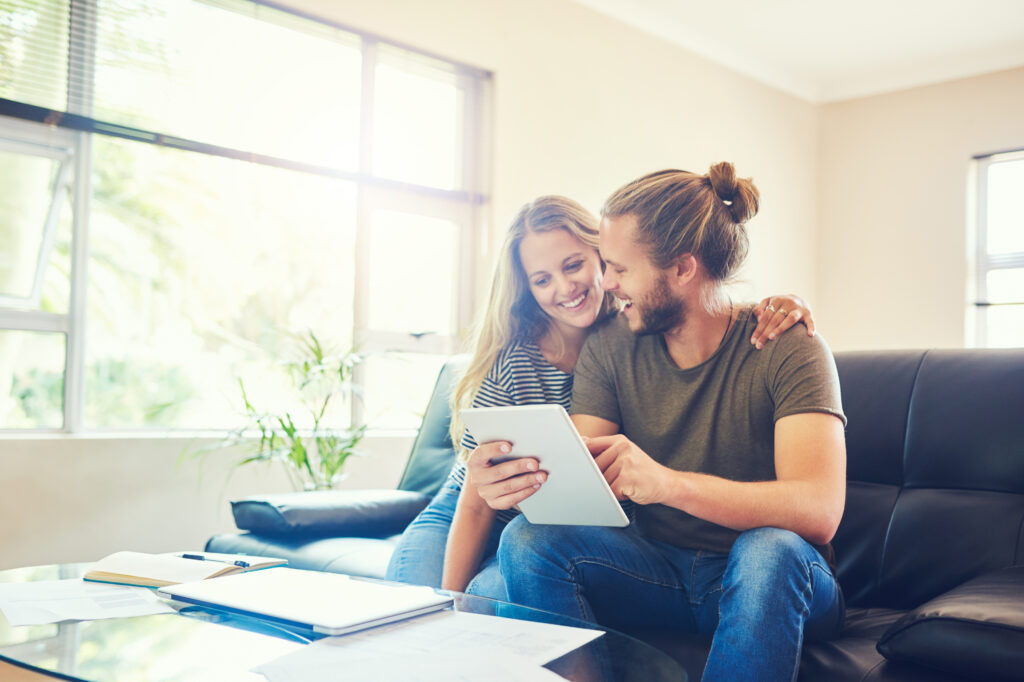 Een stel bekijkt samen een tablet in een moderne woonkamer, wat symbool staat voor het belang van een opstalverzekering om hun woning te beschermen.