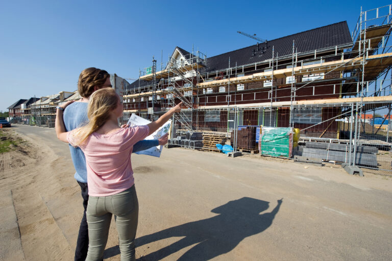 Stel bekijkt bouwplaats van nieuwbouwwoningen en wijst naar hun toekomstige huis tijdens de bouwfase