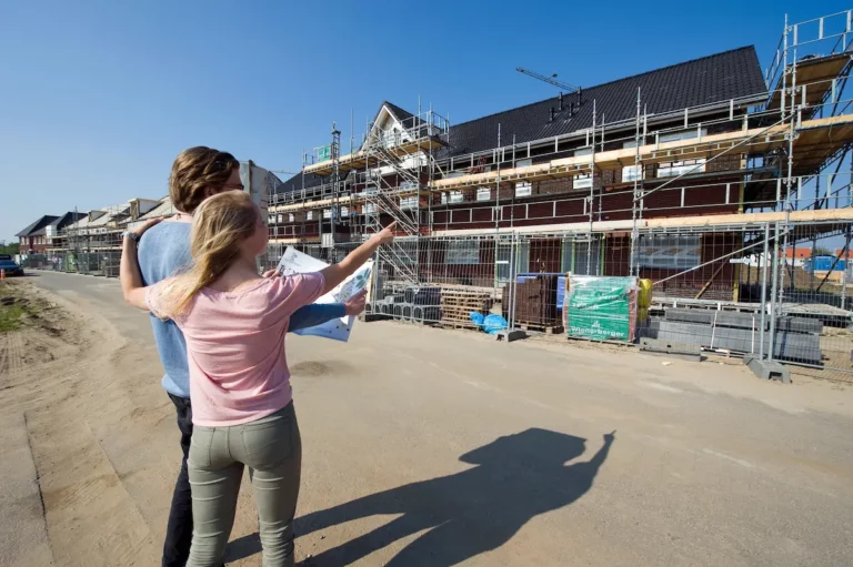 Stel bekijkt bouwplaats van nieuwbouwwoningen en wijst naar hun toekomstige huis tijdens de bouwfase