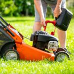 Persoon vult een oranje grasmaaier met brandstof op een grasveld.