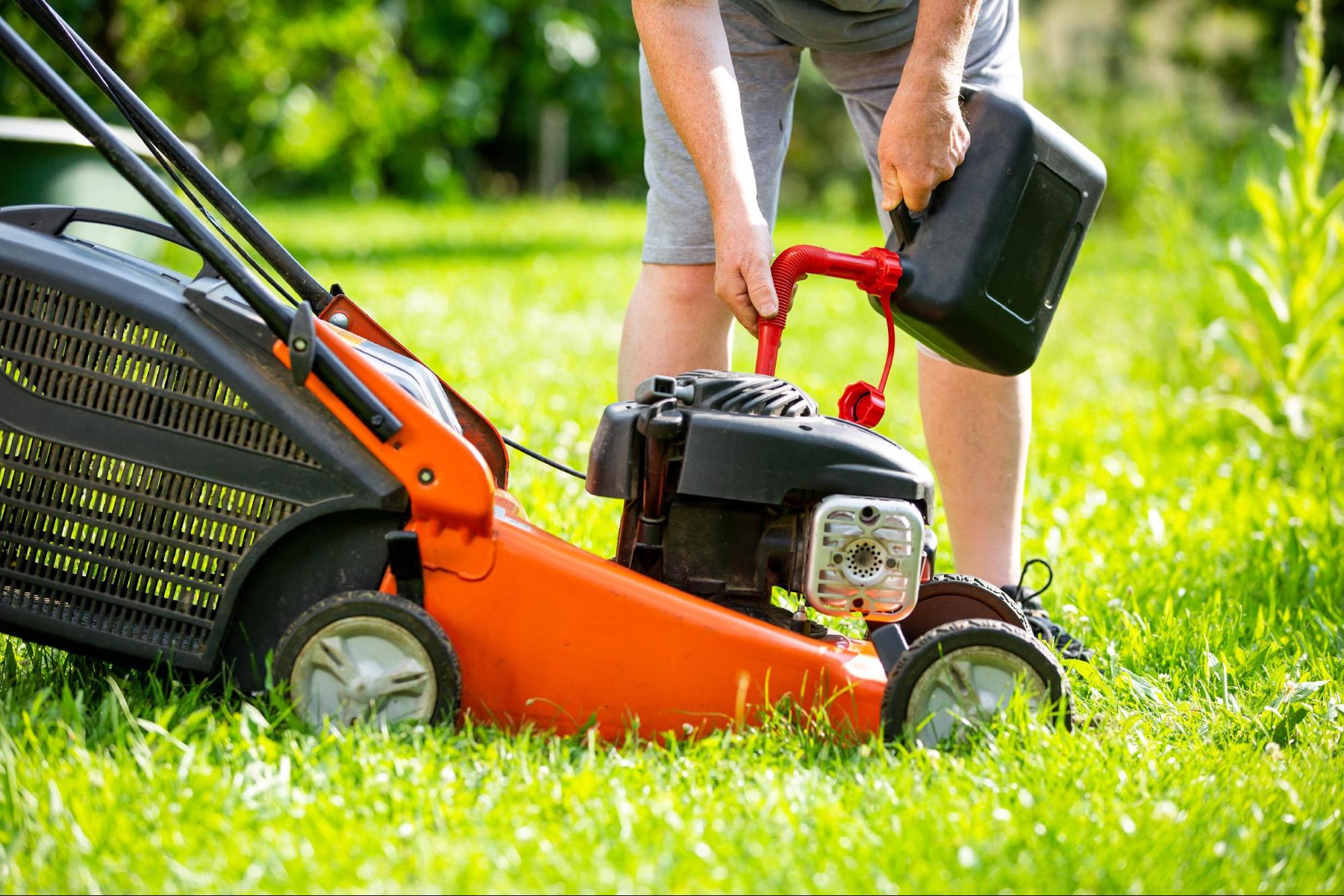 Persoon vult een oranje grasmaaier met brandstof op een grasveld.