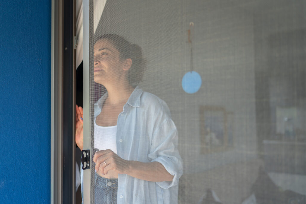 Vrouw kijkt door een deur met een handige hor, genietend van frisse lucht zonder insecten in huis.