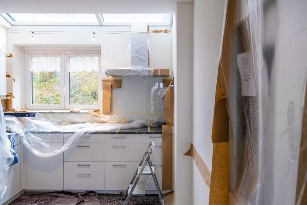 Keuken in renovatie met afgedekte werkbladen, afzuigkap en een ladder in de hoek.