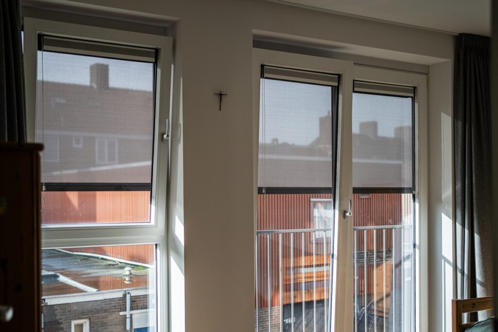 Interieur van een kamer met slimme zonwering op de ramen, die het binnenkomende zonlicht verzacht terwijl de buitenkant van het gebouw zichtbaar is.