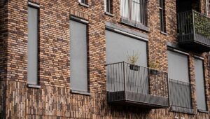 Gevel van een modern gebouw met slimme zonwering geïnstalleerd op meerdere ramen, naast balkons met plantenbakken.