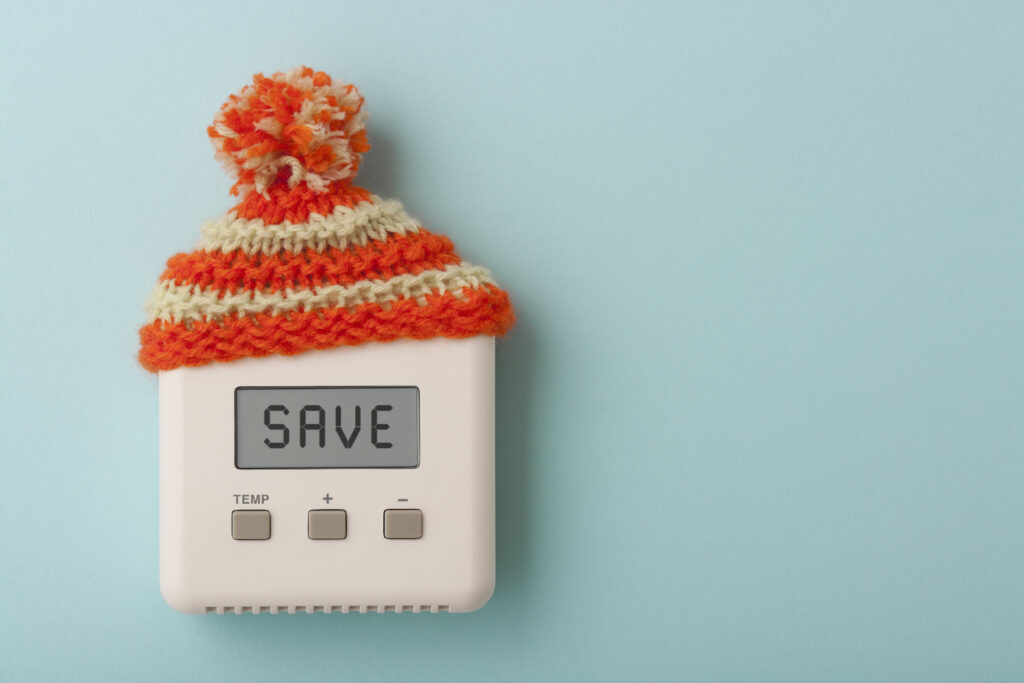 Een thermostaat met de tekst 'SAVE', voorzien van een gebreid mutsje, symboliseert manieren om de energierekening te verlagen