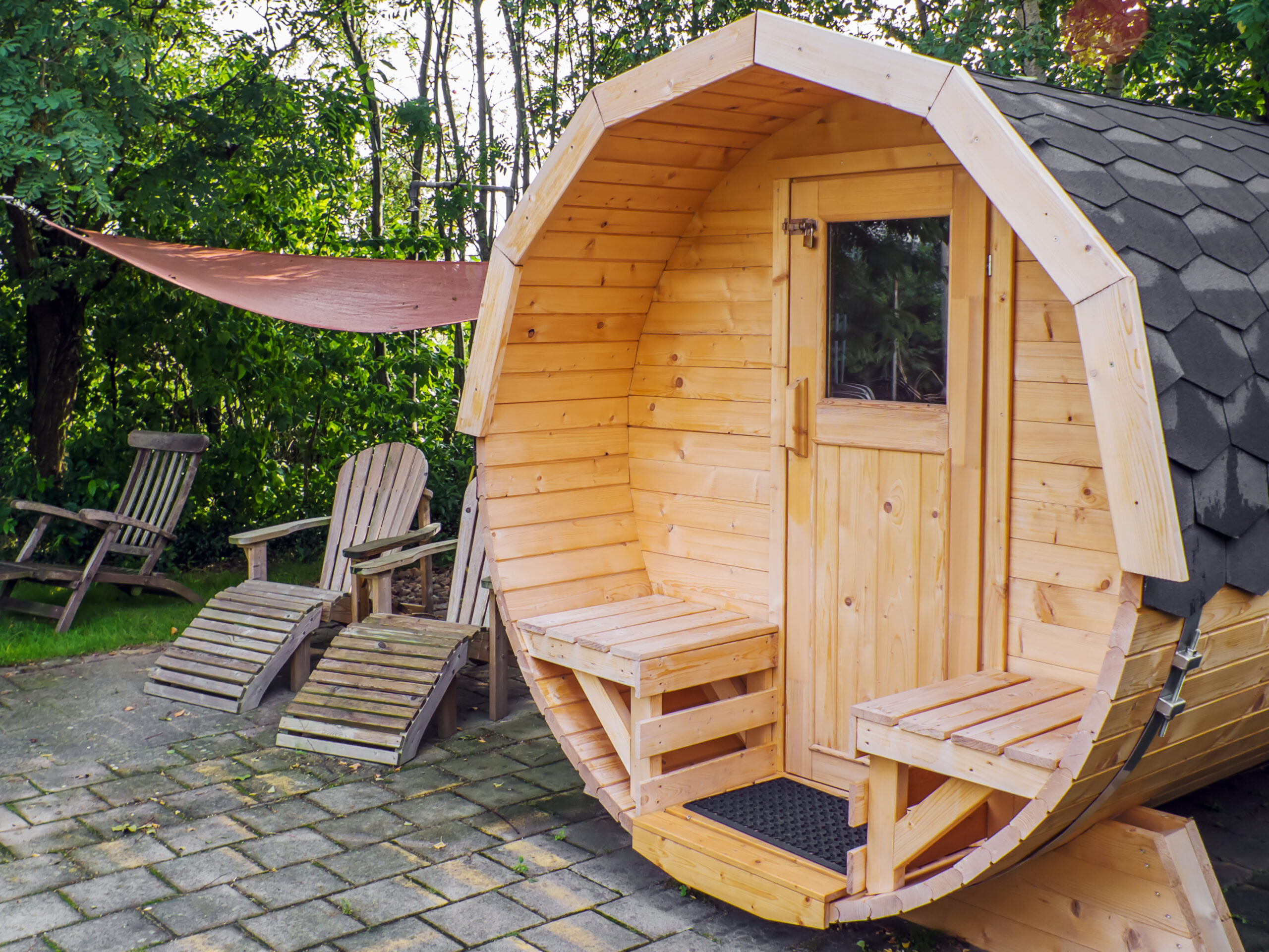 Houten buiten sauna met ligstoelen in een groene tuinomgeving