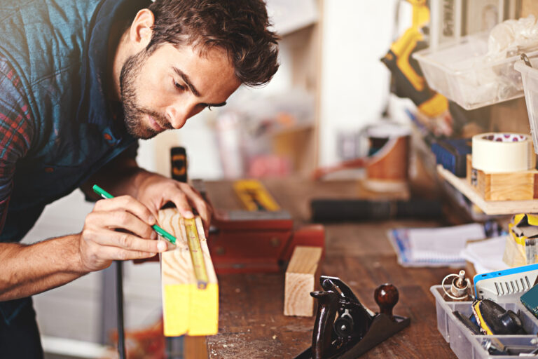 Vakman die geconcentreerd hout afmeet en markeert in een werkplaats vol gereedschap