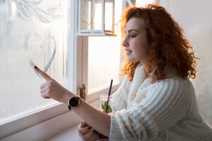 Vrouw tekent een hartje op een beslagen raam, een herinnering aan het belang van ventileren voor een gezond binnenklimaat.