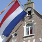 Nederlandse vlag met oranje wimpel wappert bij een karakteristieke woning met historische gevel en bouwjaar 1892.