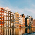 Grachtenpanden in Amsterdam weerspiegelen in het water, gefotografeerd op een zonnige dag. Een herkenbaar beeld van de Nederlandse woningmarkt, waar stijgende huizenprijzen grote gevolgen hebben voor kopers en huurders.