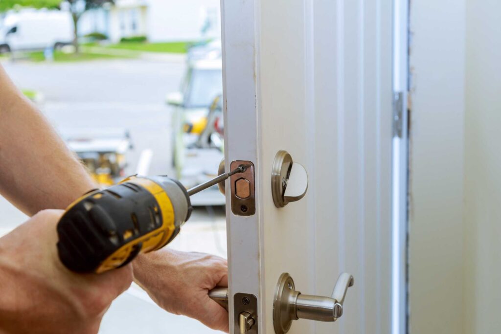 Hand van een slotenmaker die een deurslot installeert met een elektrische schroevendraaier op een witte deur, gericht op veiligheid en beveiliging.