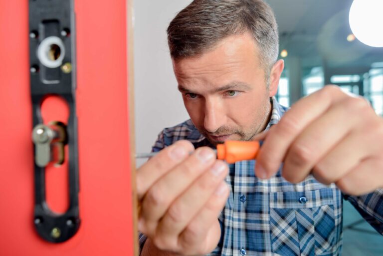 Slotenmaker aan het werk met het installeren van een cilinderslot in een rode deur, gefocust op precisie.