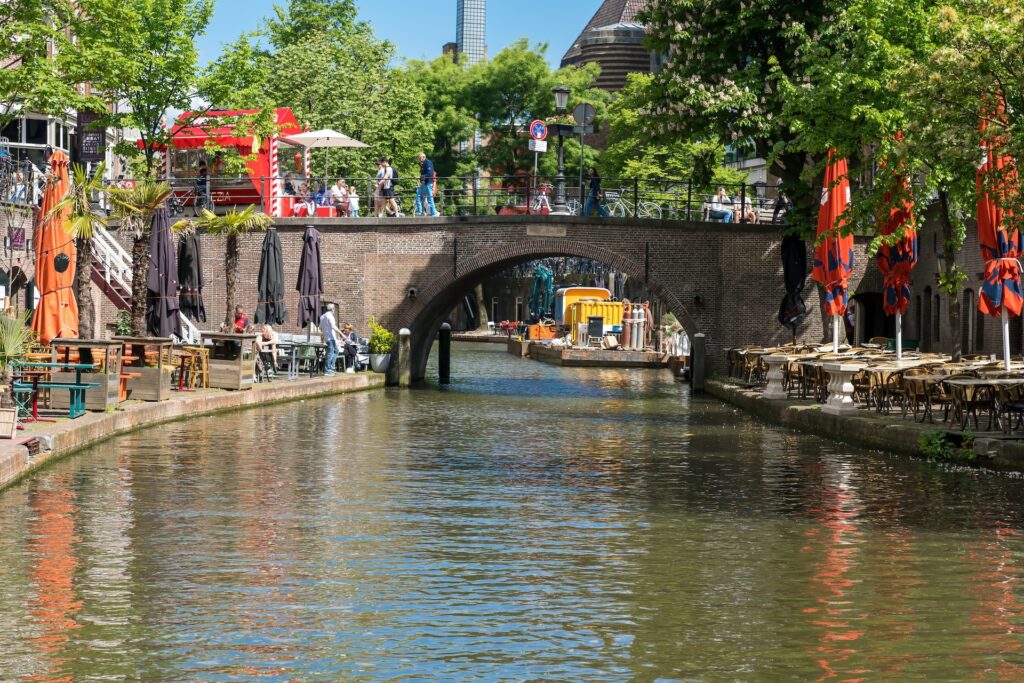 Terrasjes aan de grachten van Utrecht met een historische brug en kleurrijke parasols op een zonnige dag.