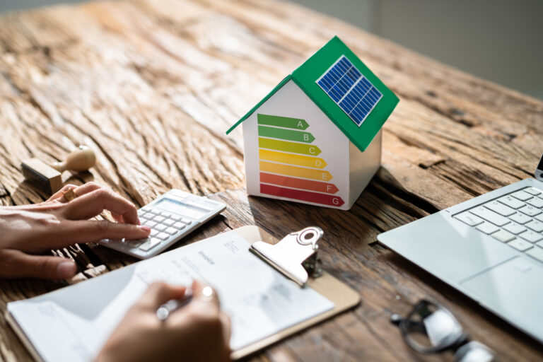 Modelhuis met energielabel en zonnepanelen, naast rekenmachine en document, symbool voor energiebesparing en financiële voordelen van isolatie