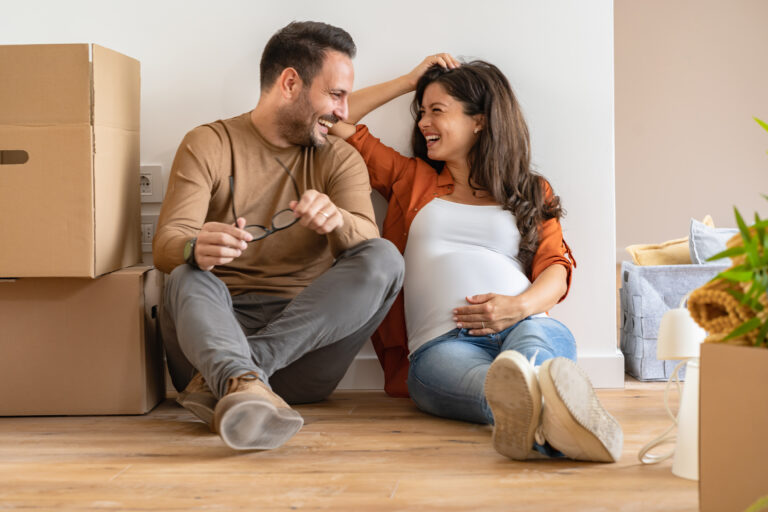 Zwanger koppel geniet van een ontspannen moment tijdens de verhuizing, zittend tussen verhuisdozen in hun nieuwe huis.