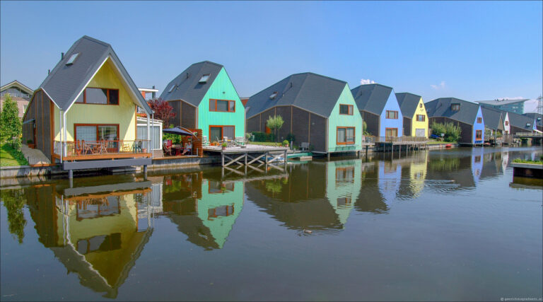 Moderne gekleurde waterwoningen in Almere met steigers en reflectie in het water, op een zonnige dag.