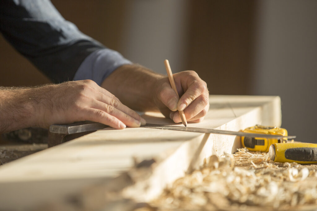 Houtbewerker markeert een rechte zaagsnede op een houten plank ter voorbereiding op het zagen met een tafelzaag.