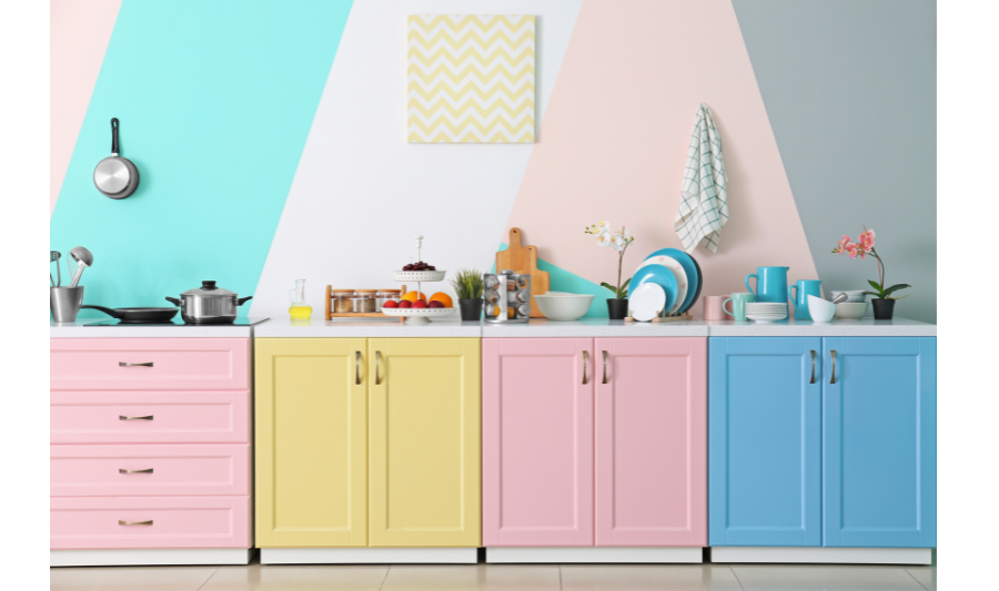 Pastelkleurige keuken met roze, gele en blauwe kastjes, gecombineerd met een speels geometrisch patroon op de muur. Een frisse en moderne interpretatie van de heropleving van pastelkleuren in het interieur.