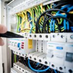 Close-up van een groepenkast met kleurrijke elektriciteitskabels en een elektricien die een schakelaar controleert