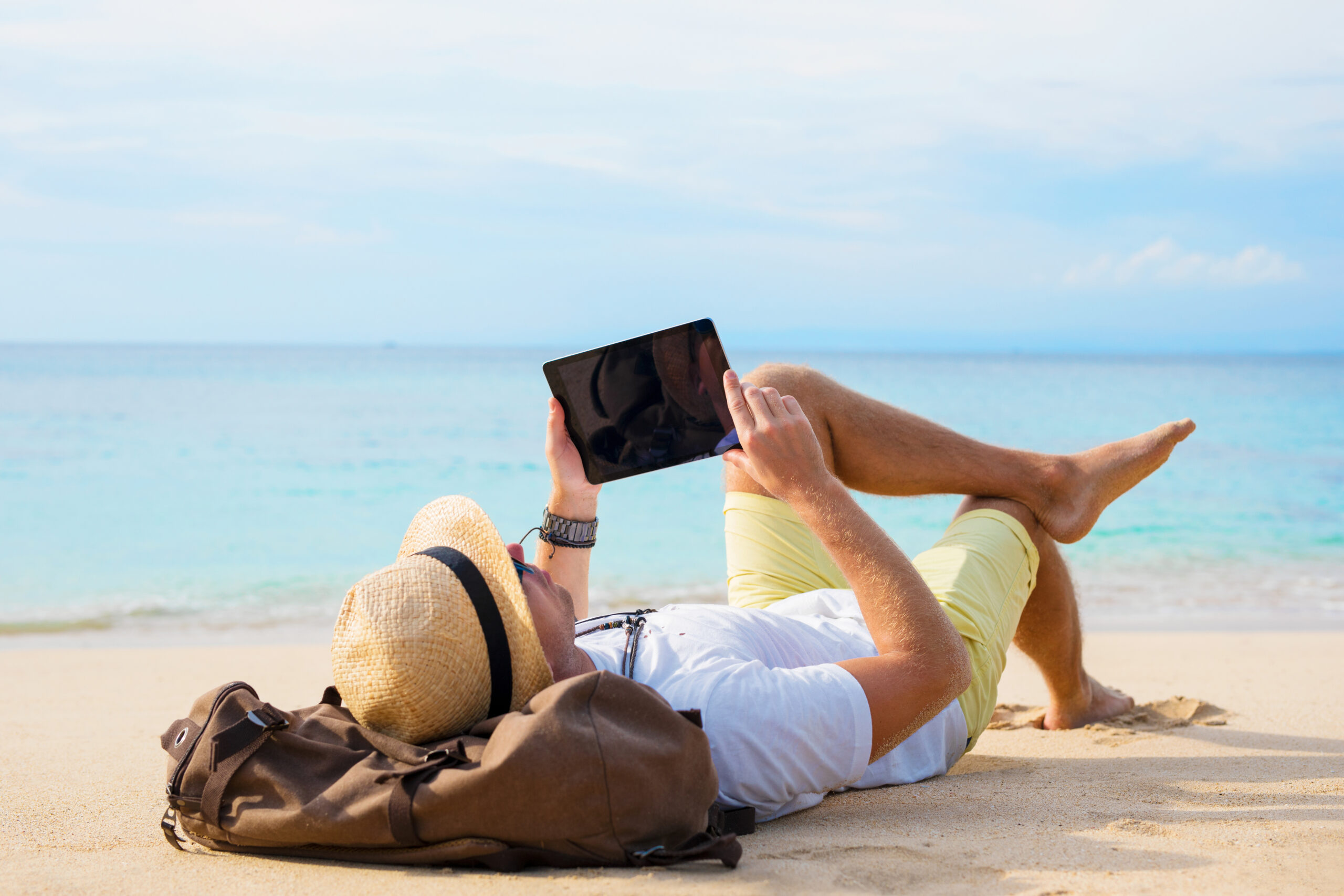 Man ontspant op het strand terwijl hij op een tablet Nederlandse TV streamt.