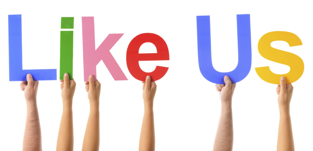 Handen houden gekleurde letters omhoog met de tekst “Like Us” – symbool voor social media en online community opbouwen.