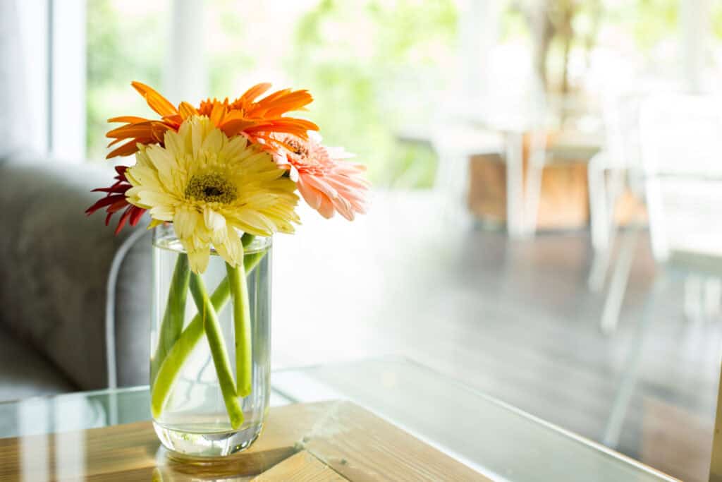 Kleurrijke bloemen in een glazen vaas op een salontafel in een lichte woonkamer