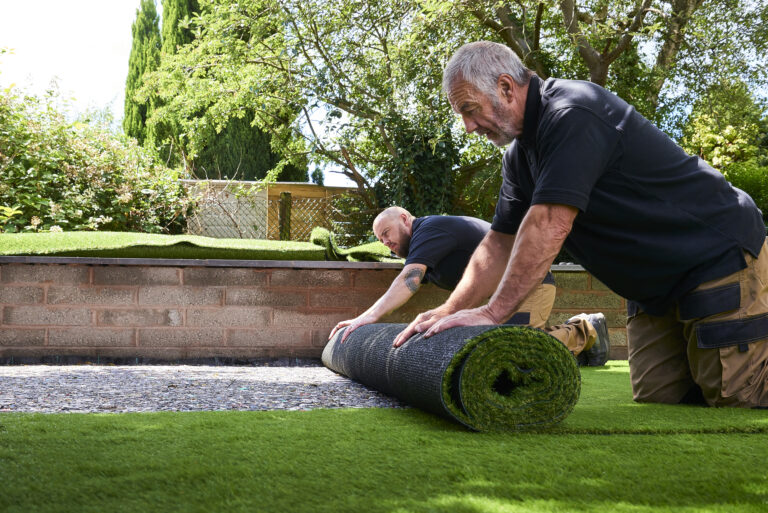 Twee vakmannen leggen kunstgras in een tuin voor een onderhoudsvriendelijk gazon.