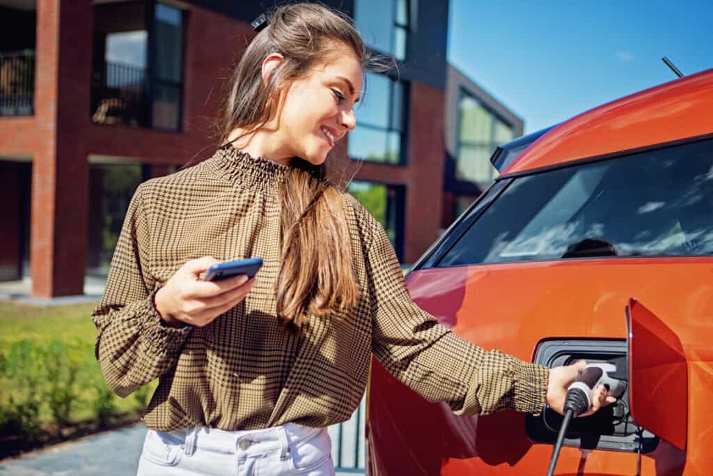 Vrouw laadt elektrische auto op bij woning met laadpaal