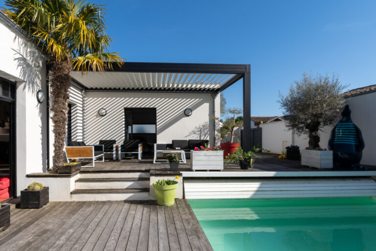 Moderne veranda met houten vlonder, stijlvolle overkapping en comfortabele loungehoek bij een zwembad.