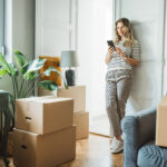 Vrouw in een lichte woonkamer met verhuisdozen tijdens de voorbereiding op een verhuizing naar een kleinere woning