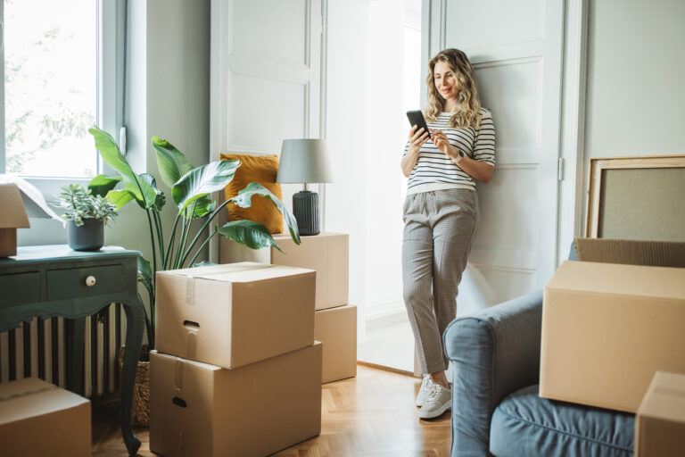 Vrouw in een lichte woonkamer met verhuisdozen tijdens de voorbereiding op een verhuizing naar een kleinere woning