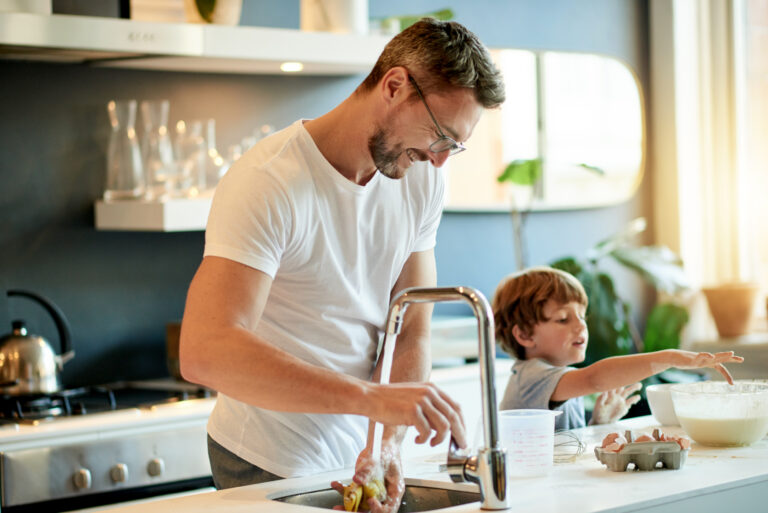 Vader wast groente onder de kraan terwijl zijn zoon helpt in de keuken, symbool voor comfortabel wonen met kalkvrij water.